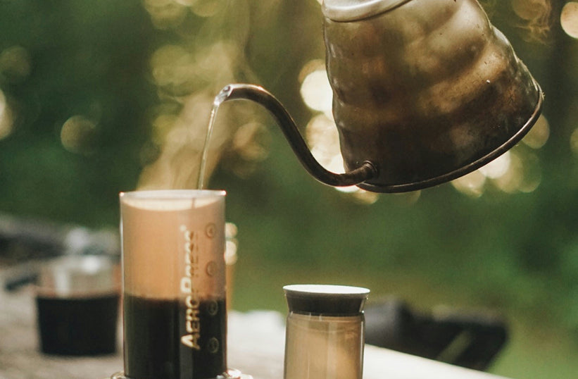AeroPress brewing coffee outdoors with a gooseneck kettle at a campsite - Seattle Coffee Gear