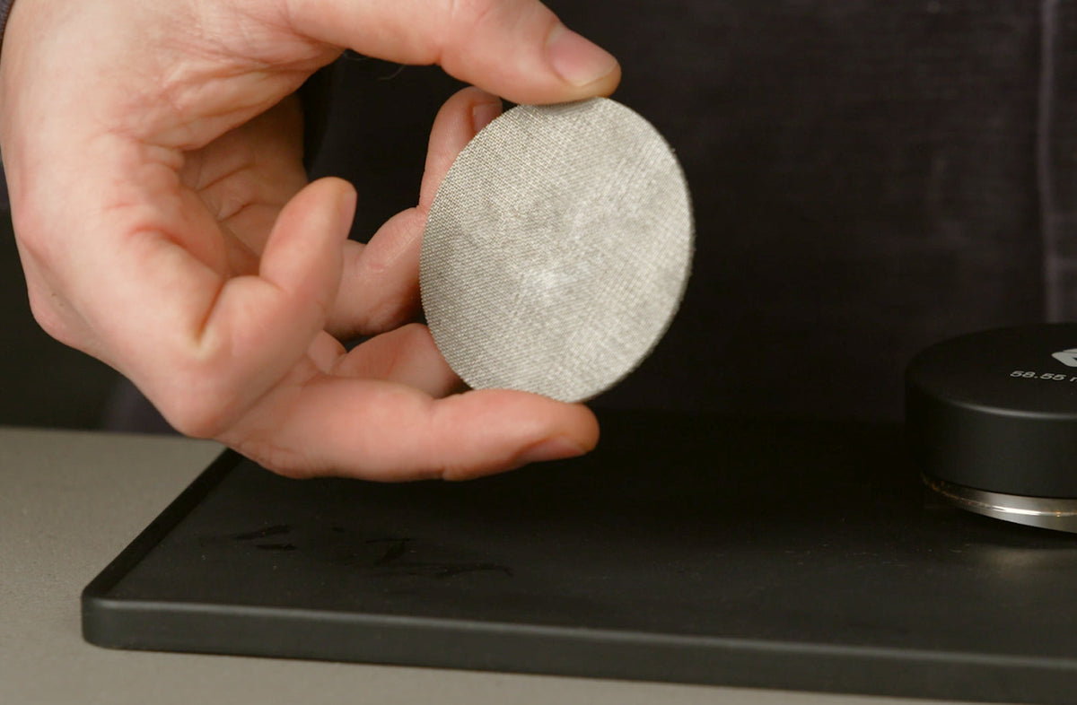 Barista holding a stainless steel espresso puck screen above a tamping mat - Seattle Coffee Gear
