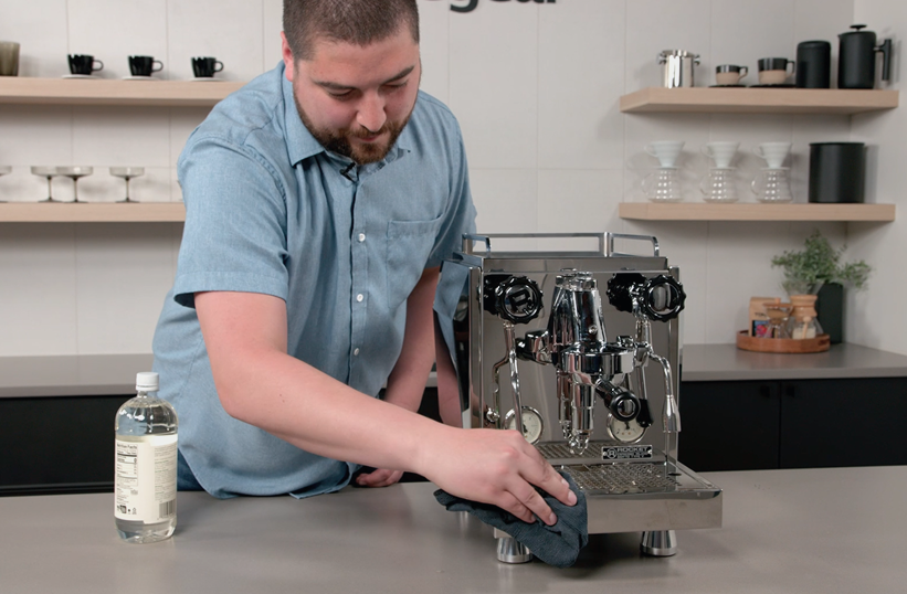 Barista wiping down a stainless steel home espresso machine with a microfiber cloth