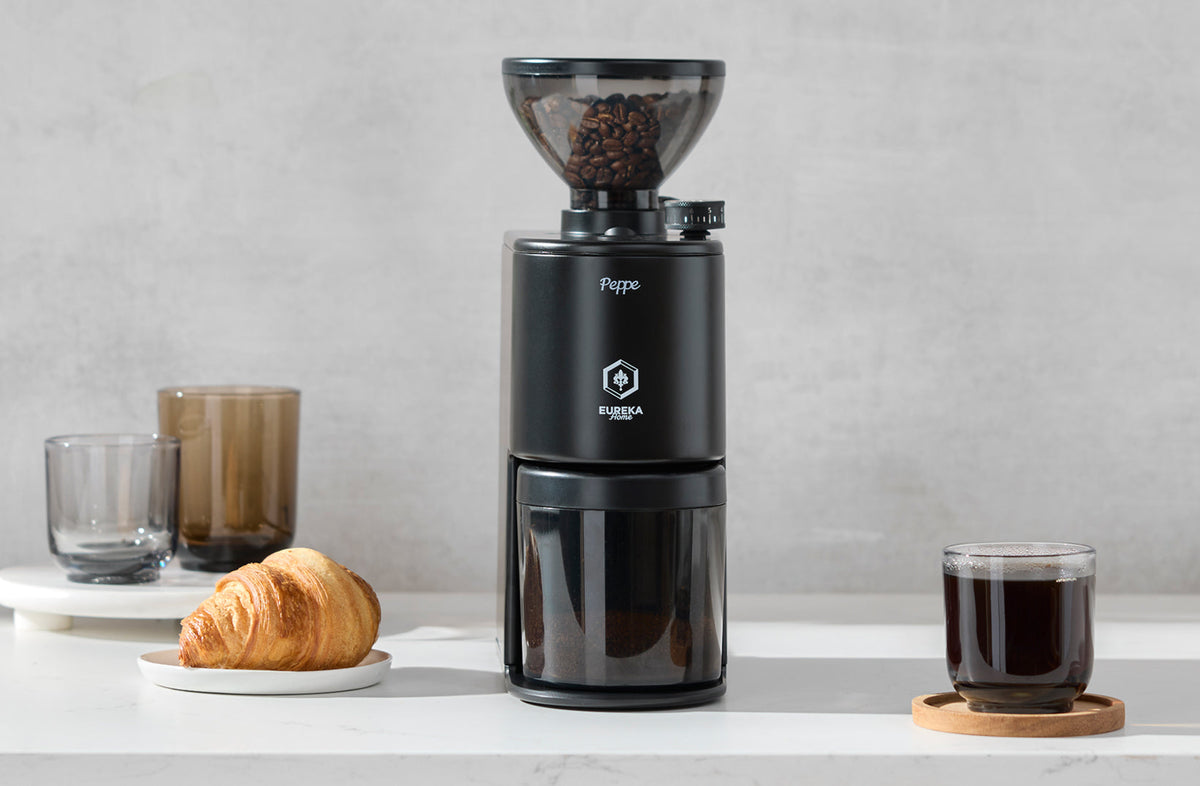 Matte black Eureka Peppe grinder on a kitchen counter beside brewed coffee and a croissant - Seattle Coffee Gear