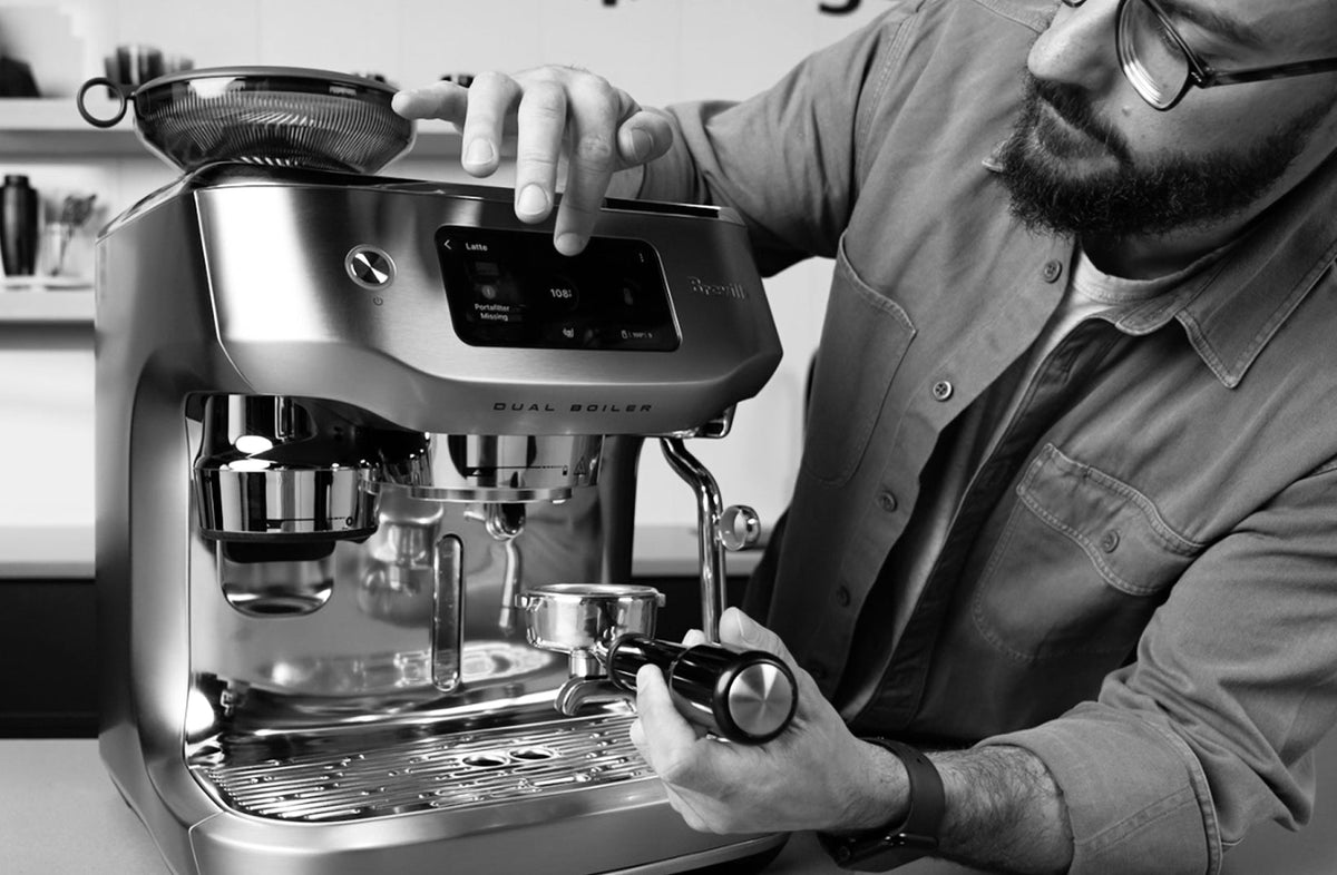 Barista adjusting a stainless steel Breville Dual Boiler espresso machine on a counter - Seattle Coffee Gear