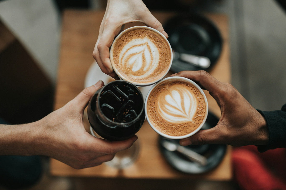 Three coffee cups being clinked together, two with latte art and one ice. Photo by Nathan Dumlao on Unsplash        - Seattle Coffee Gear